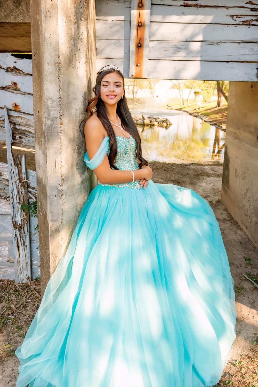 Ethereal aqua ballgown photographed against rustic weathered wall with golden sunlight.