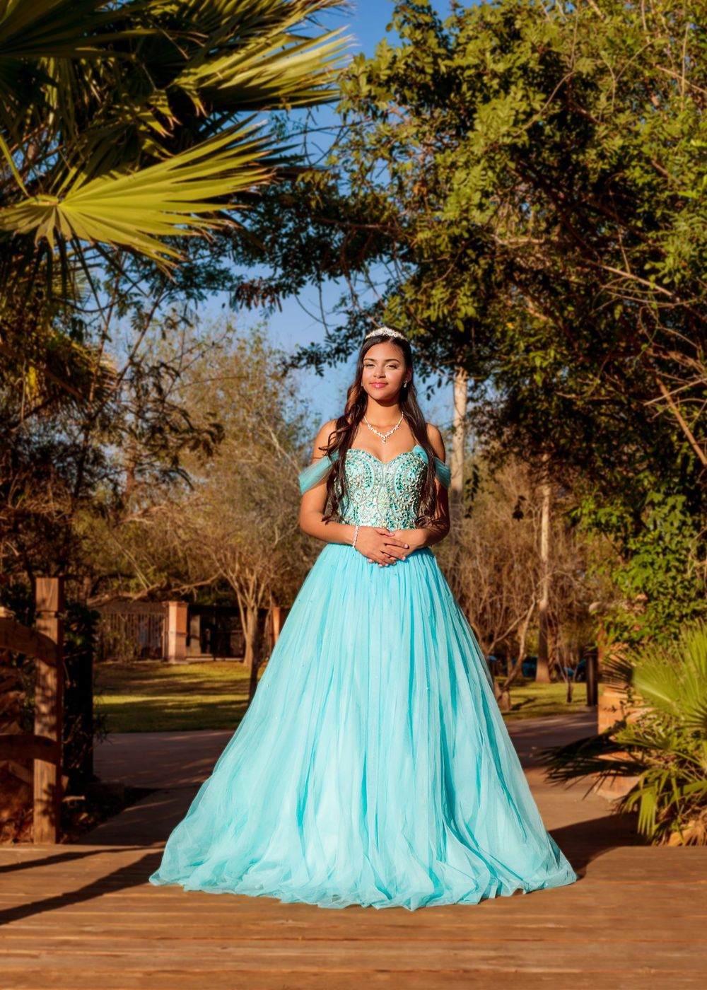 A stunning aqua blue ball gown photographed in a tropical garden setting with palm trees and natural lighting.