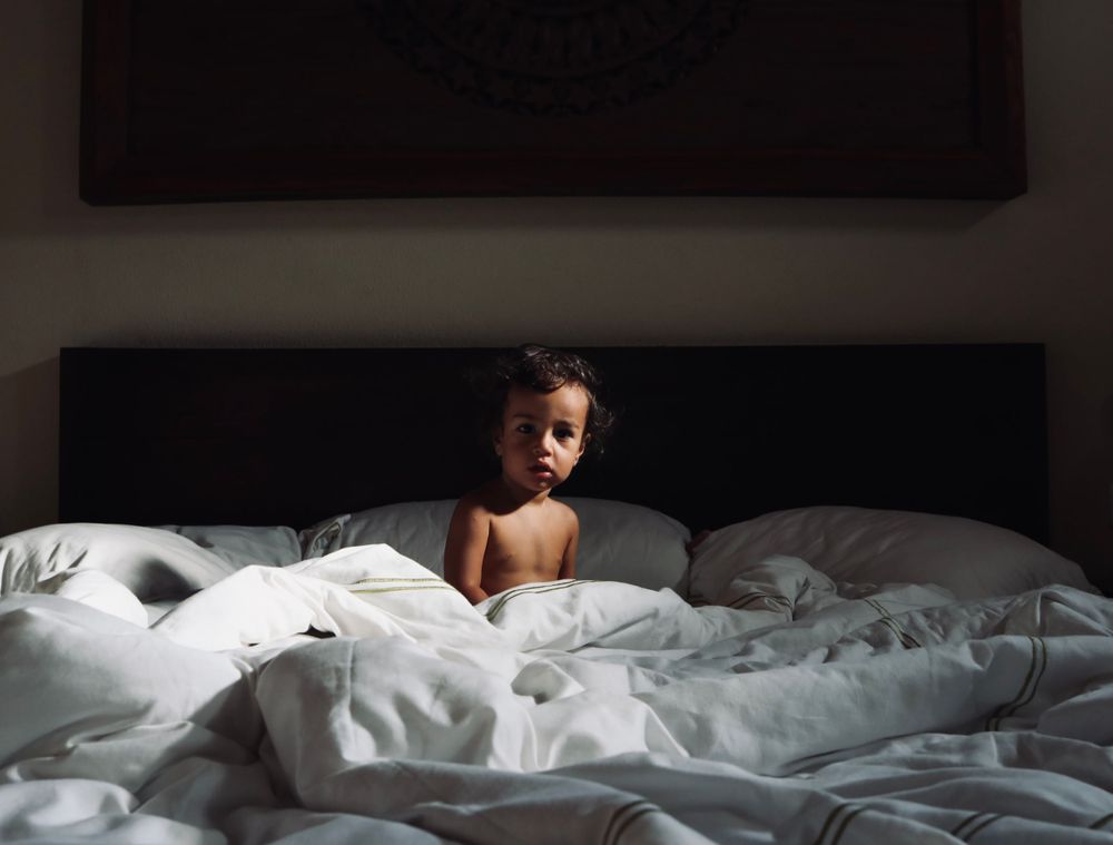 Unmade bed with rumpled white sheets and bedding in dim lighting.