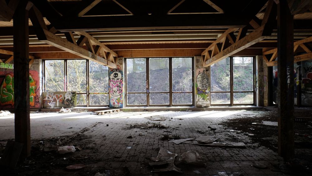 Interior of an abandoned industrial building with broken windows and debris.