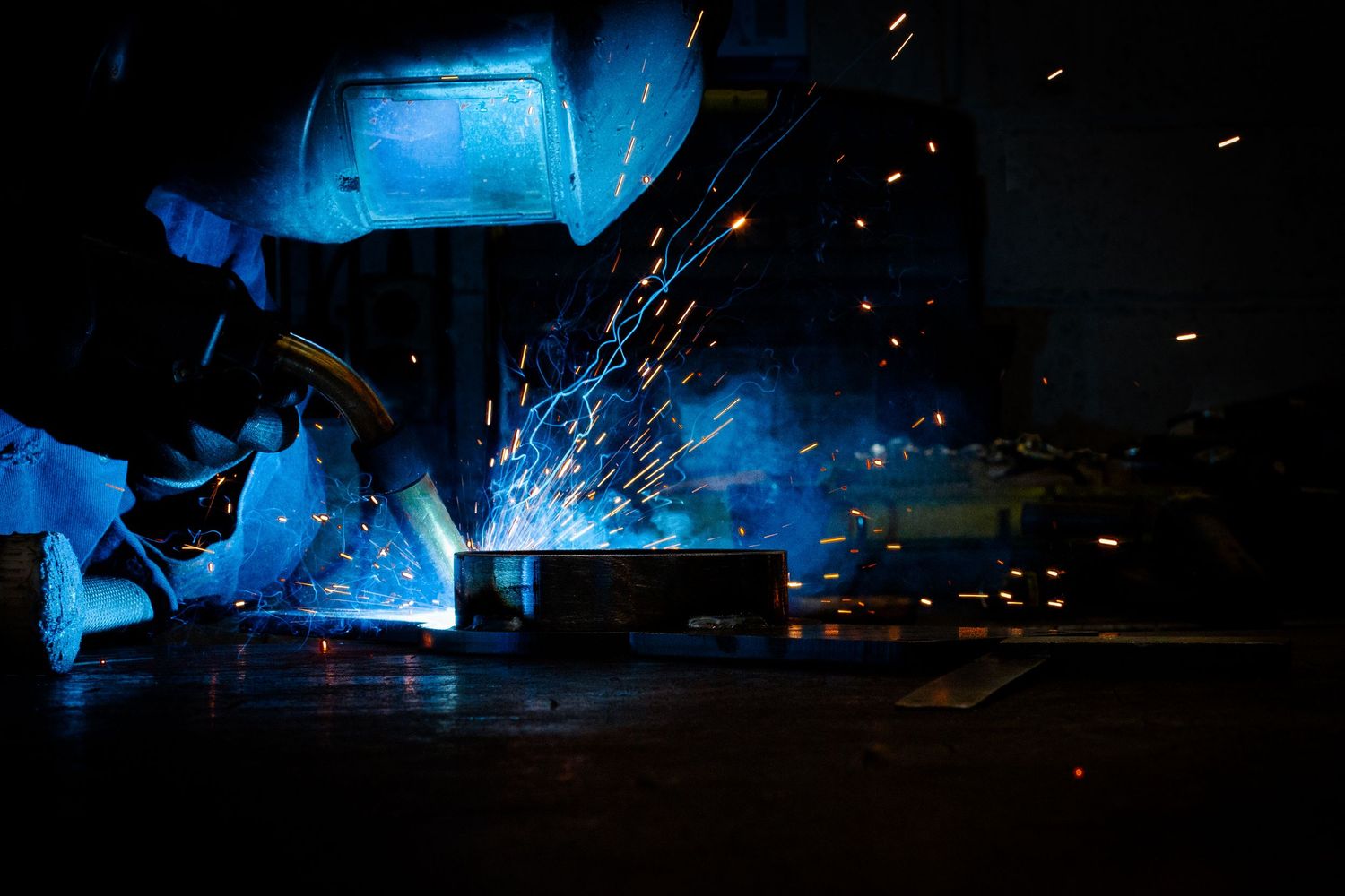Arc welding process creating brilliant blue light and showering sparks in dark workshop.
