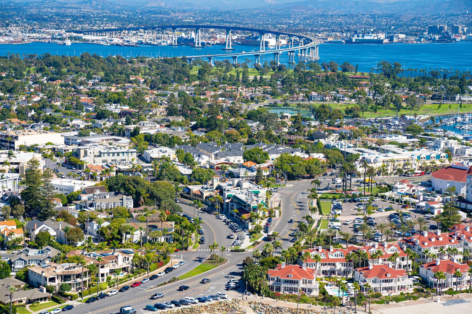 Scenic aerial view of Southern California coastal homes, winding streets, and the iconic San Diego-Coronado Bridge over the water.