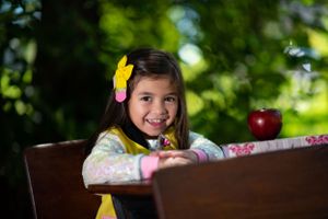 A student sits at a wooden desk with an apple and yellow flower accent.