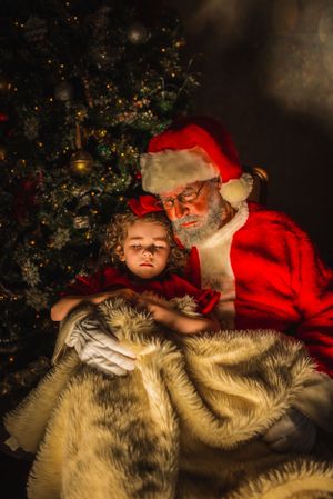A magical Christmas scene with Santa and a child reading by a decorated tree.