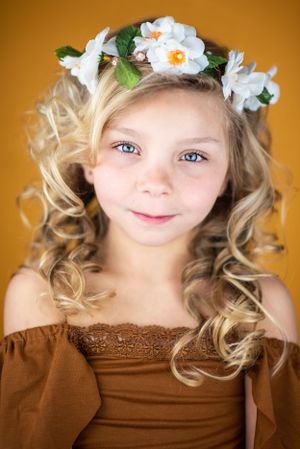 Portrait showing curled blonde hair adorned with white flowers against an orange backdrop.