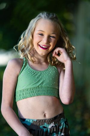 A dancer in green athletic wear poses outdoors with a bright expression.