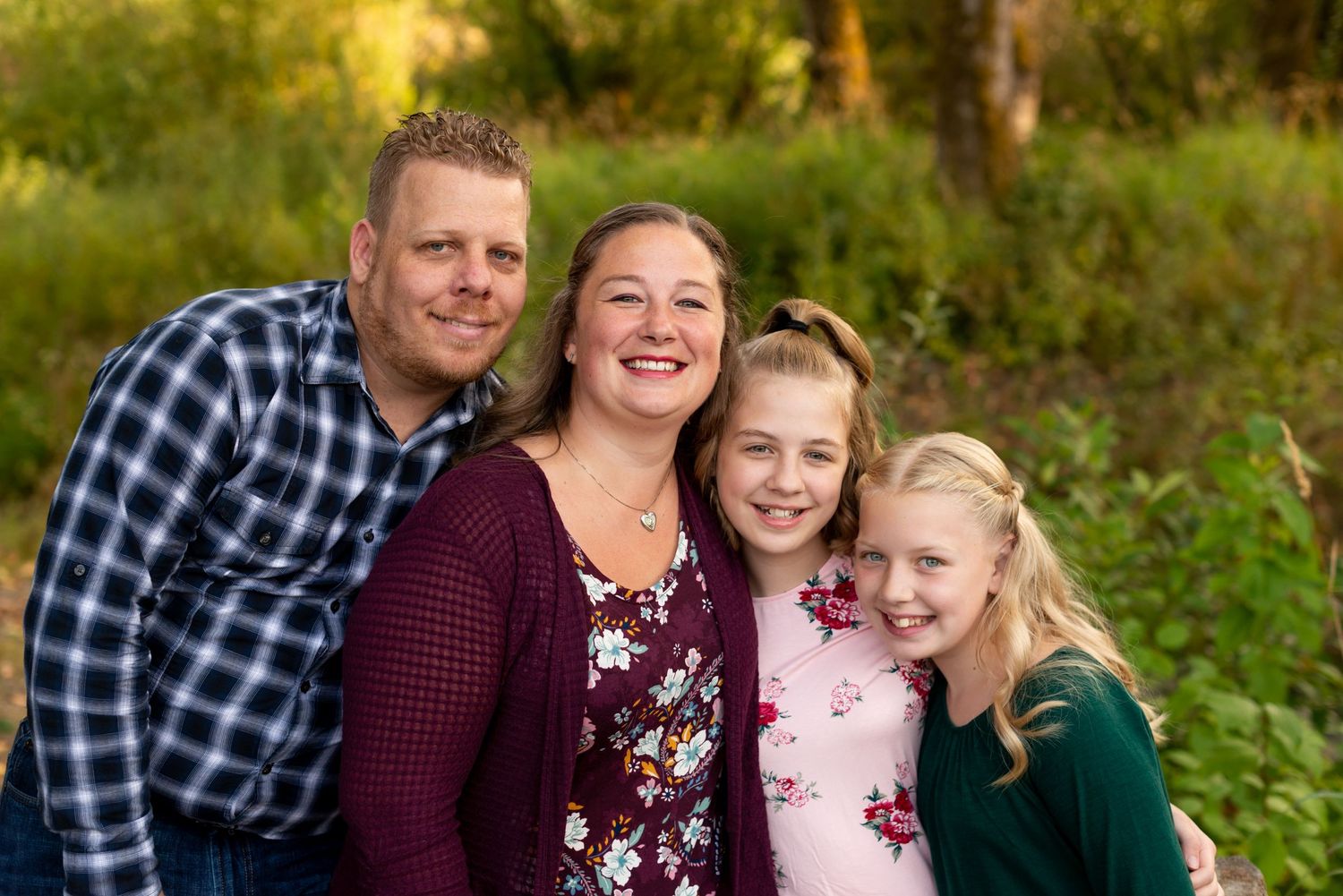 A cheerful family poses together outdoors in casual attire against a natural green background.
