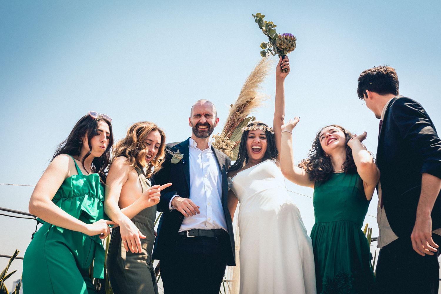 Joyful wedding group poses together with arms raised in celebration.