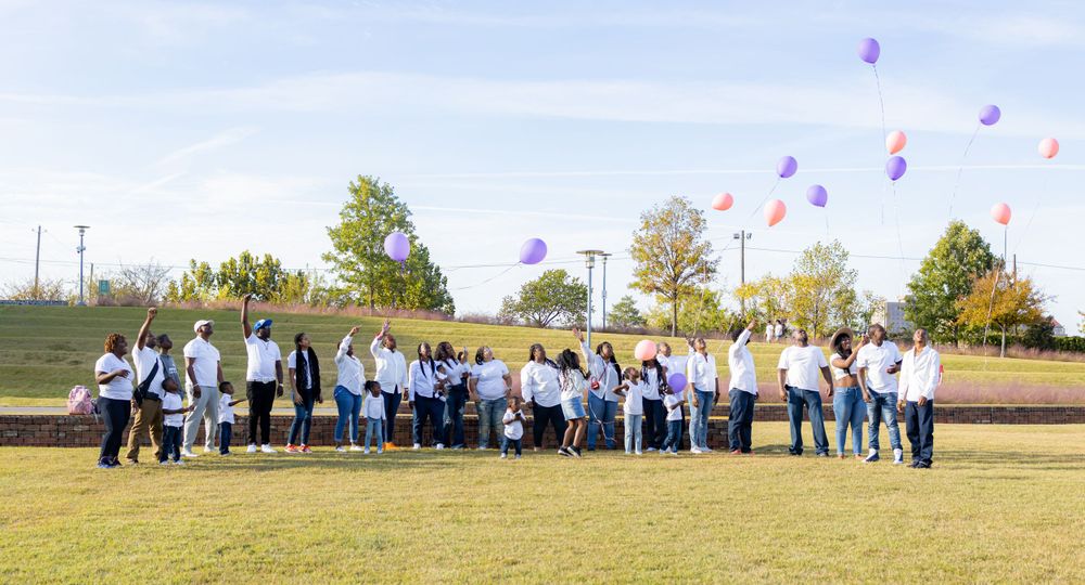 Large group releasing purple balloons into the sky during an outdoor celebration.