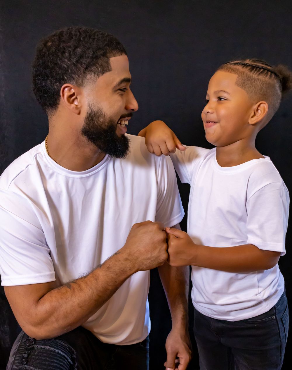 Parent and child in white t-shirts share playful moment against dark background.
