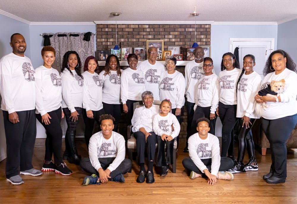 A large family group wearing matching white shirts poses together for a formal portrait in a home setting.