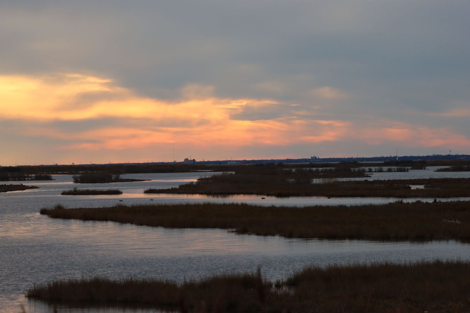Peaceful coastal marsh wetlands at sunset with golden orange clouds reflecting over calm tidal waterways.