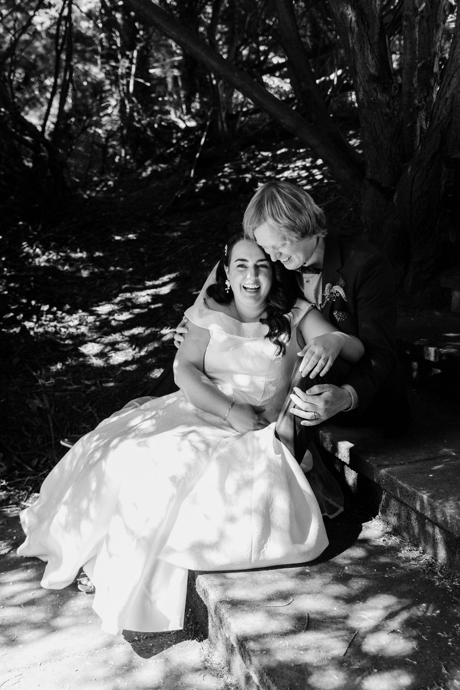 A sweet black and white portrait of young couple sitting together in dappled sunlight.