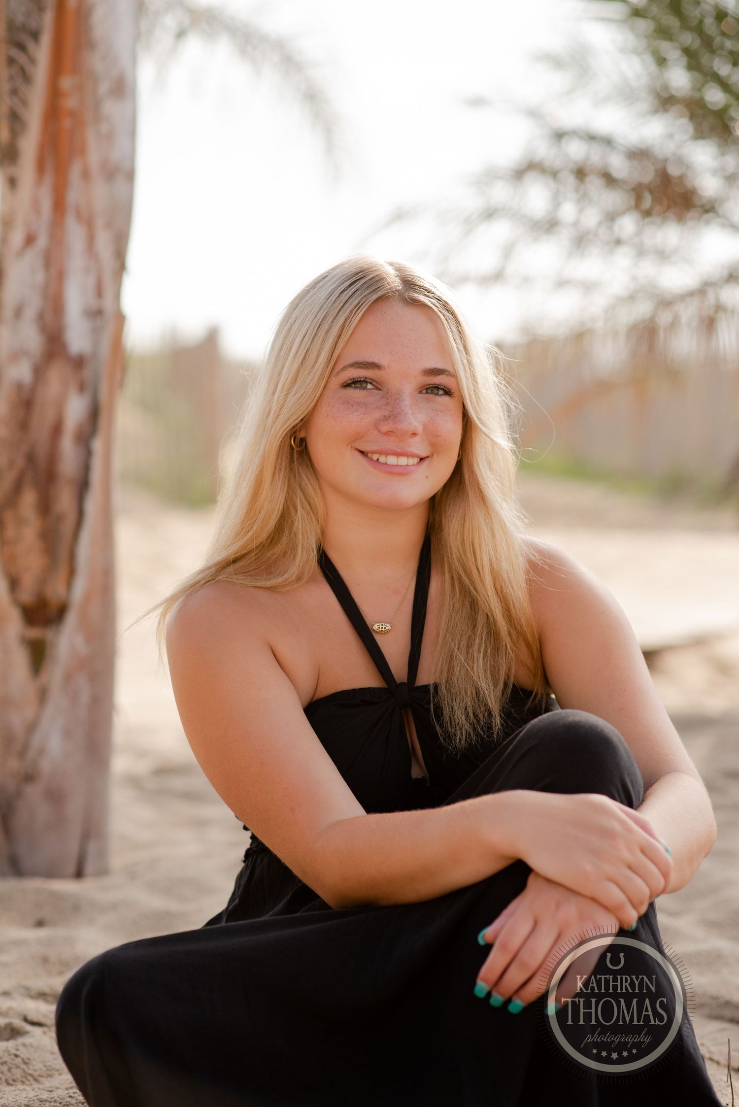 Outdoor portrait by palm tree wearing black halter dress with natural lighting.