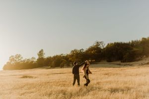 Two silhouettes running through a golden field at sunset.