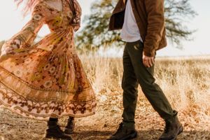 Close up of flowing floral dress and boots walking through tall grass at sunset.