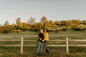 Romantic couple sharing an intimate moment by a rustic fence during golden hour in an autumn field.