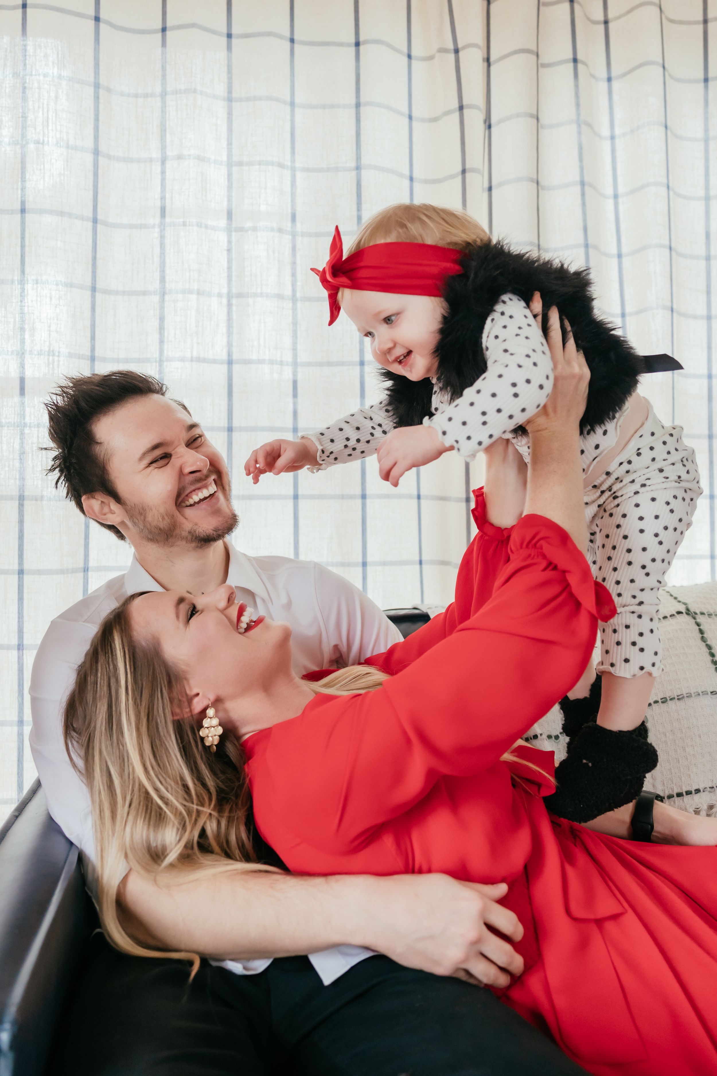 A playful indoor family moment with bright red and polka dot outfits on a dark couch.