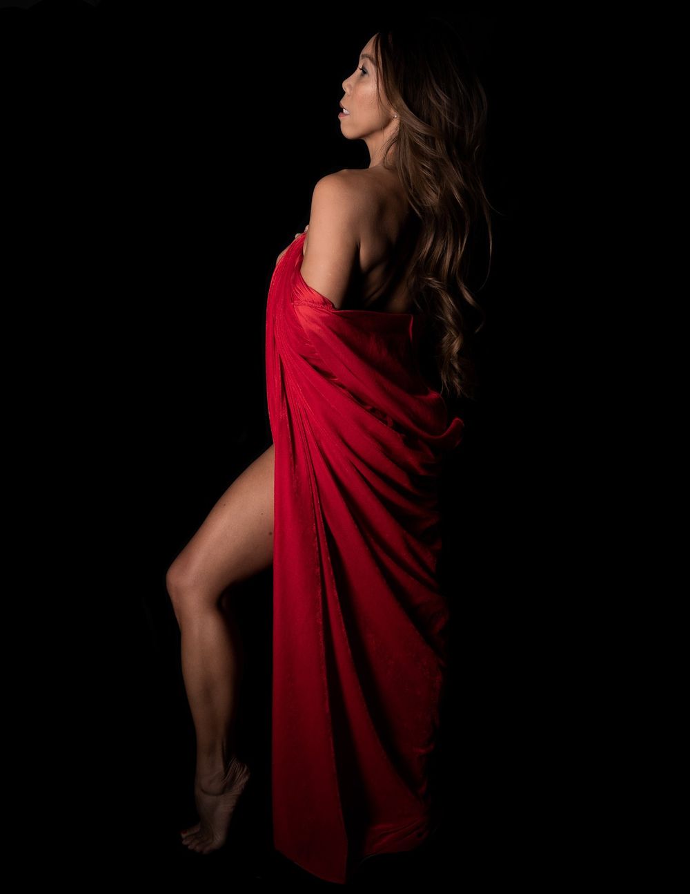 Elegant silhouette draped in flowing red fabric against black background.
