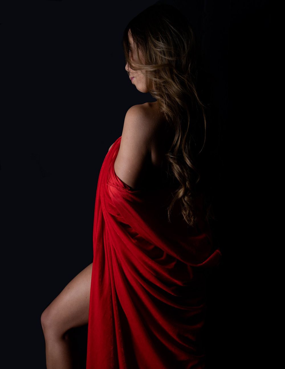 Artistic side profile wrapped in flowing red fabric with dramatic lighting.