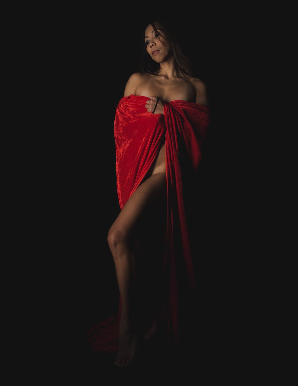 Graceful pose in draped red fabric against dark studio backdrop.