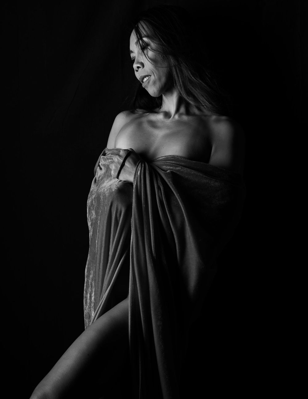 Artistic black and white portrait of figure draped in dark fabric against black background.