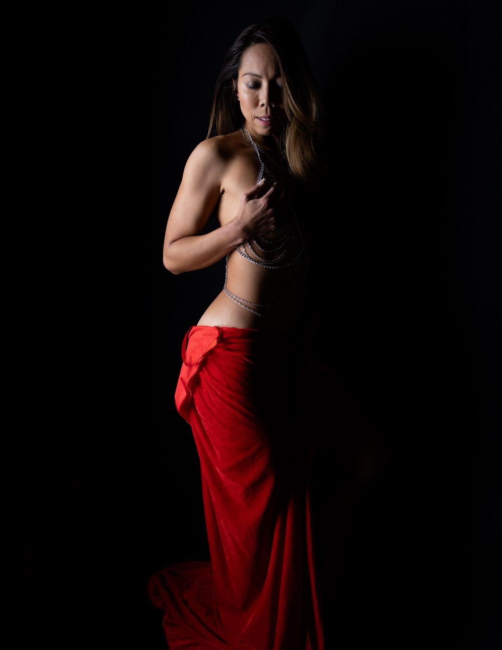 Figure poses in red skirt with dramatic lighting and dark backdrop.