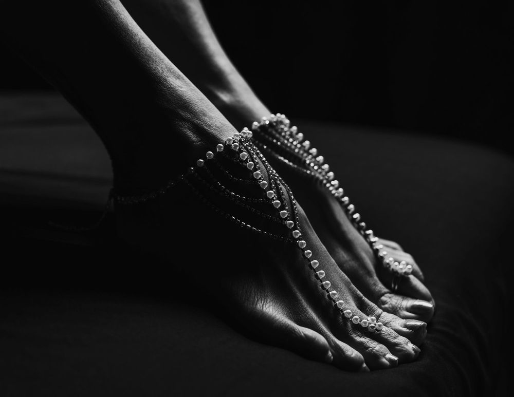 Black and white detail of feet adorned with beaded jewelry chains.