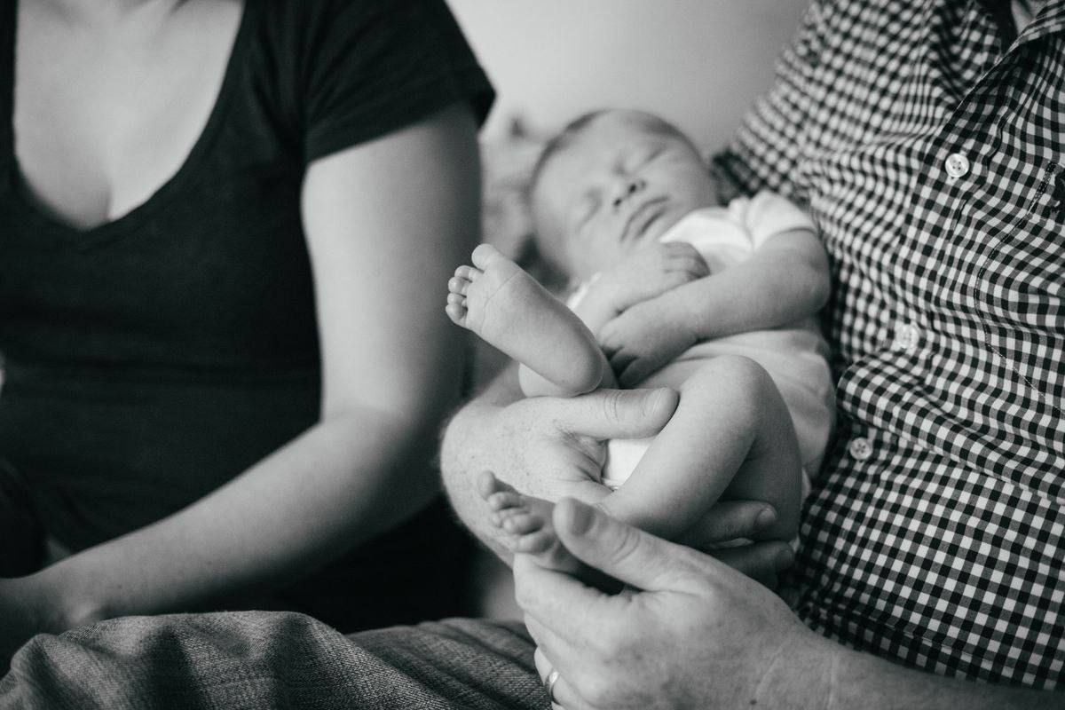 Black and white image of sleeping newborn baby being cradled in gentle arms.
