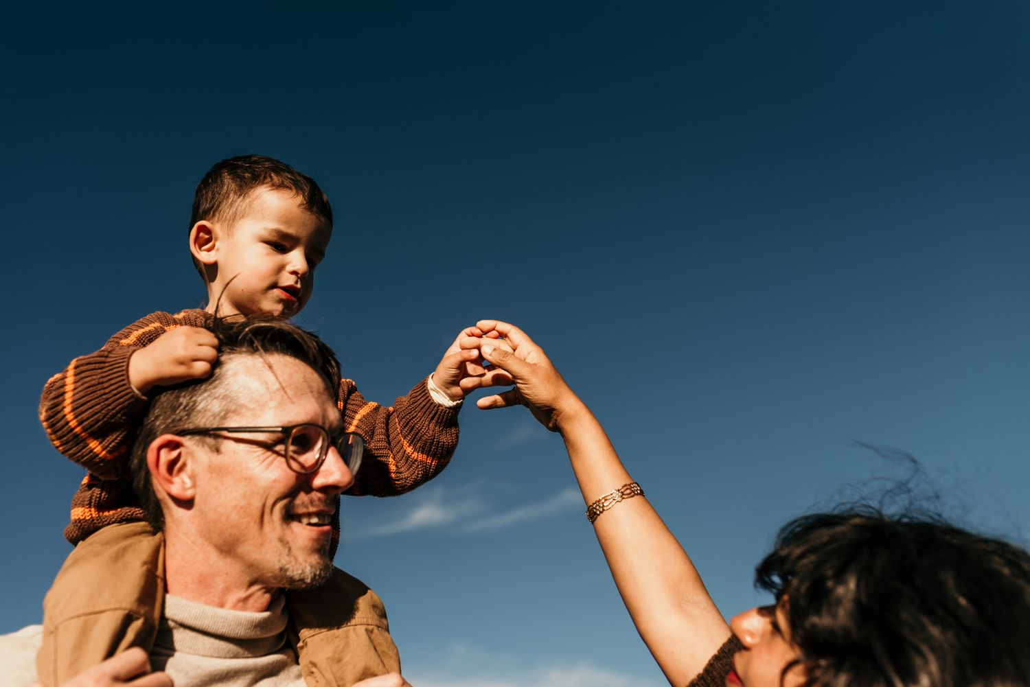 Joyful outdoor family moment captured against blue sky during golden hour.