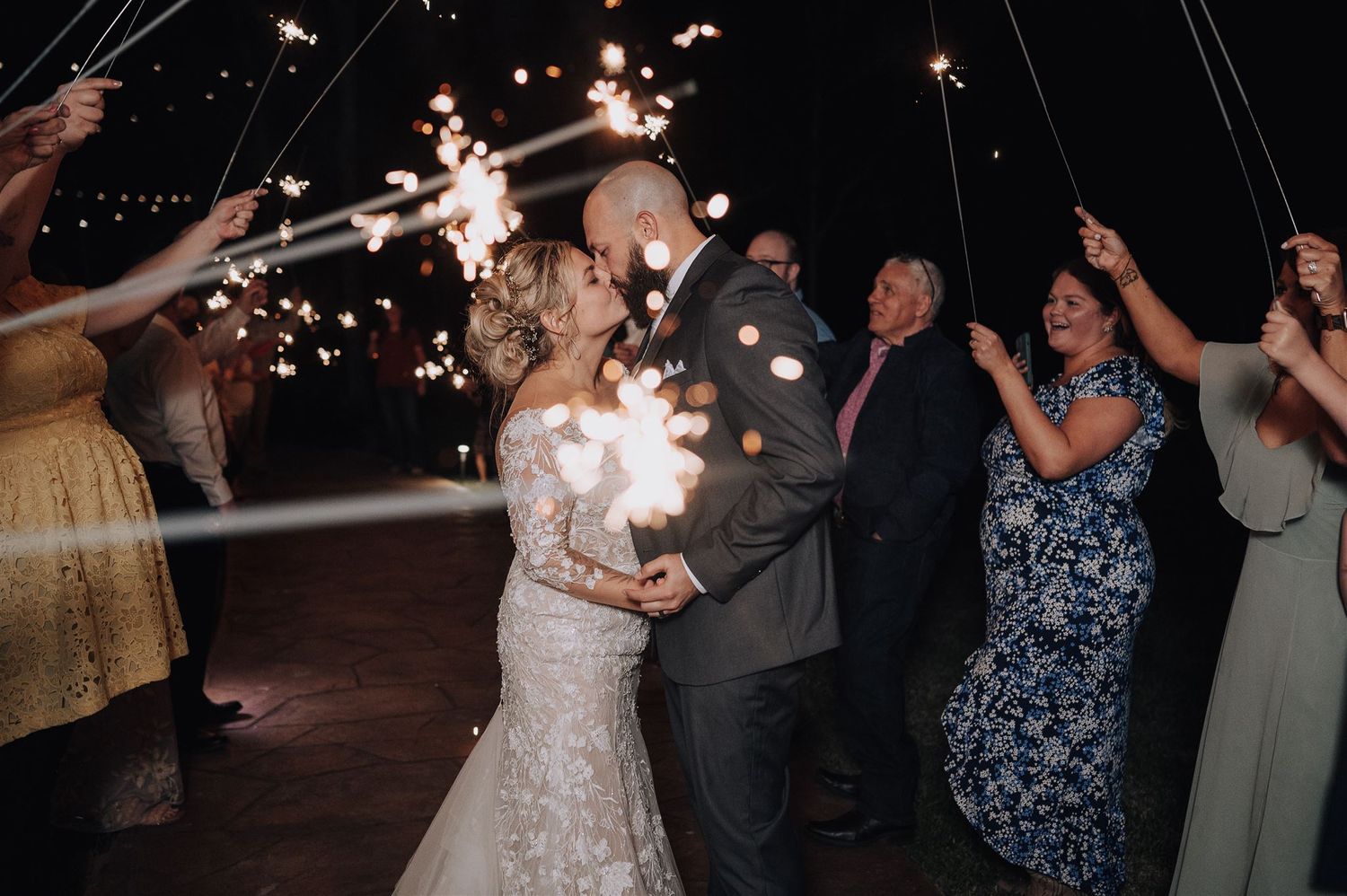 Couple shares intimate dance moment under sparkler lights at evening reception.