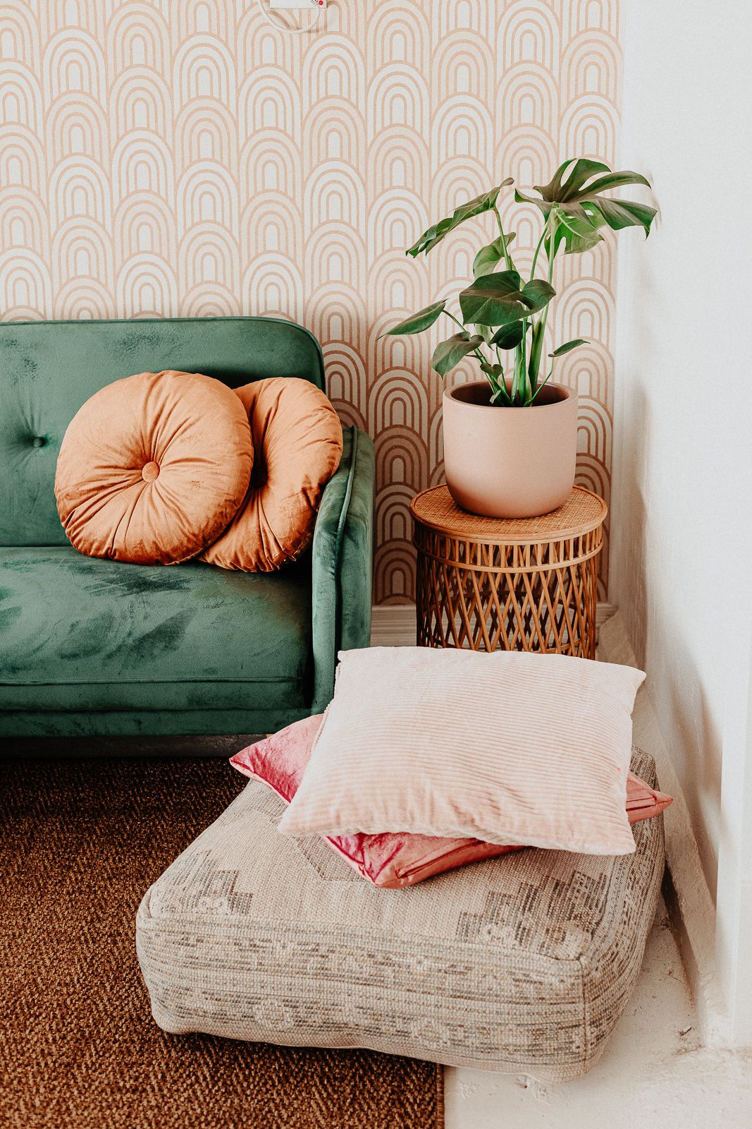 Cozy living room corner with green velvet sofa, round rattan side table, and peach accent pillows.