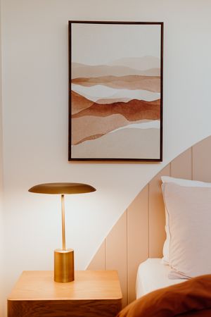 Modern bedroom decor with abstract landscape art and gold table lamp on wooden nightstand.