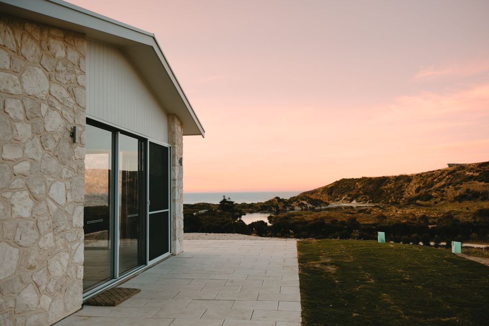 Modern stone building with large windows at sunset against pink sky.