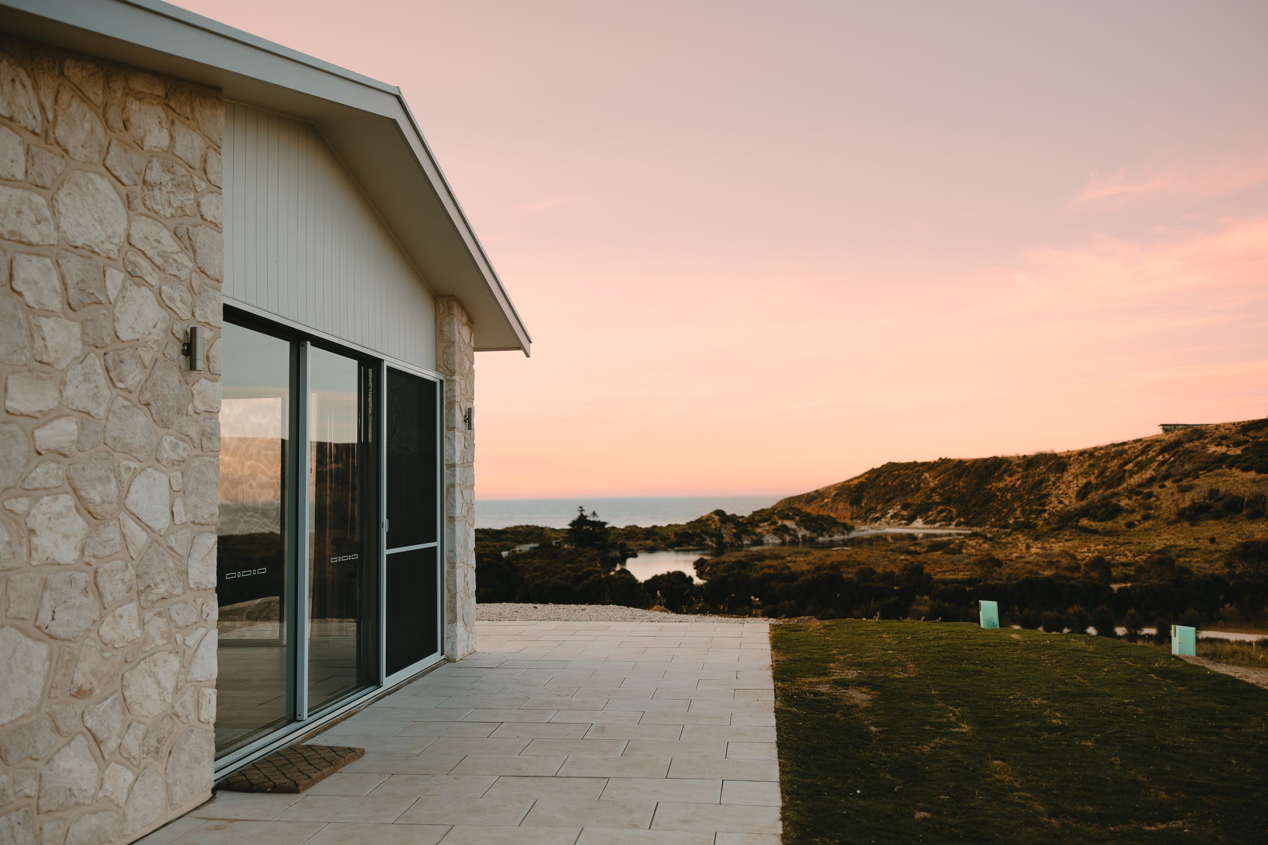 Modern stone building with large windows at sunset against pink sky.