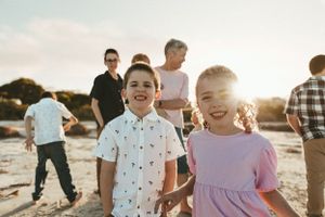 Children playing and laughing on the beach at sunset with adults in the background.