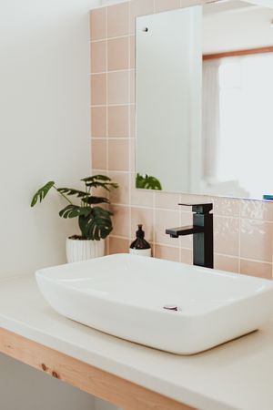 Contemporary bathroom featuring a vessel sink, black faucet, and pink tile accents.