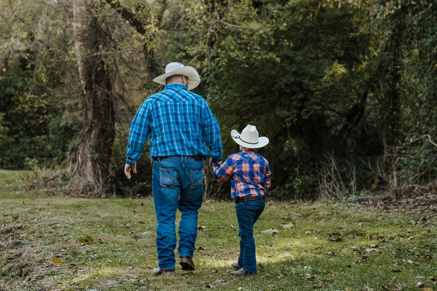 A father and son walk together wearing cowboy hats at a family photography session in Northwest Missouri.