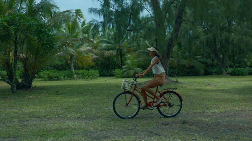 Person rides orange bicycle through lush tropical garden setting.