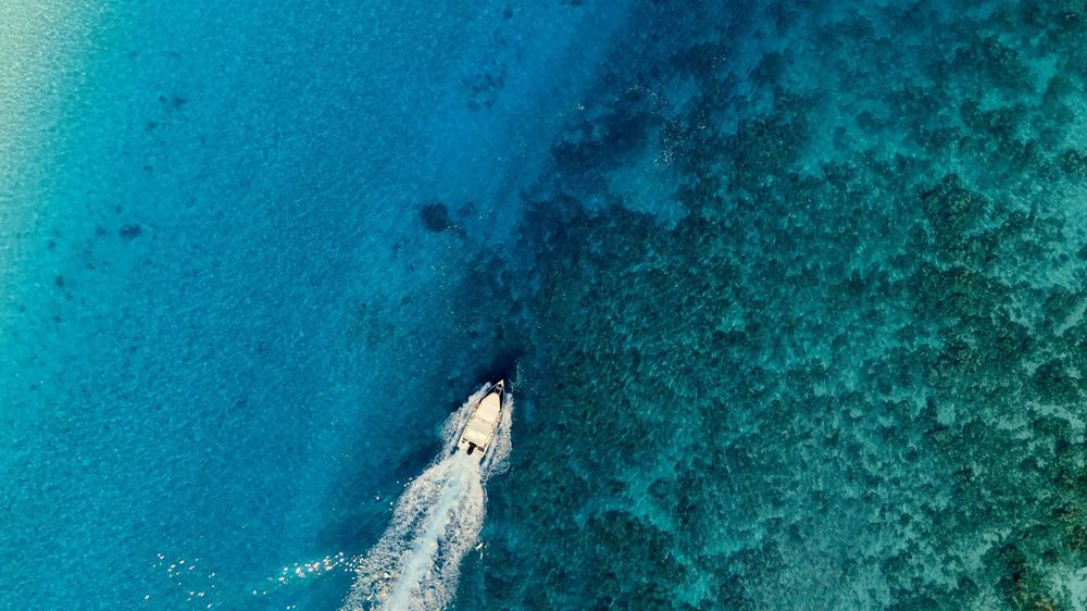 Aerial view of a boat creating wake patterns in crystal clear turquoise waters near a coral reef.
