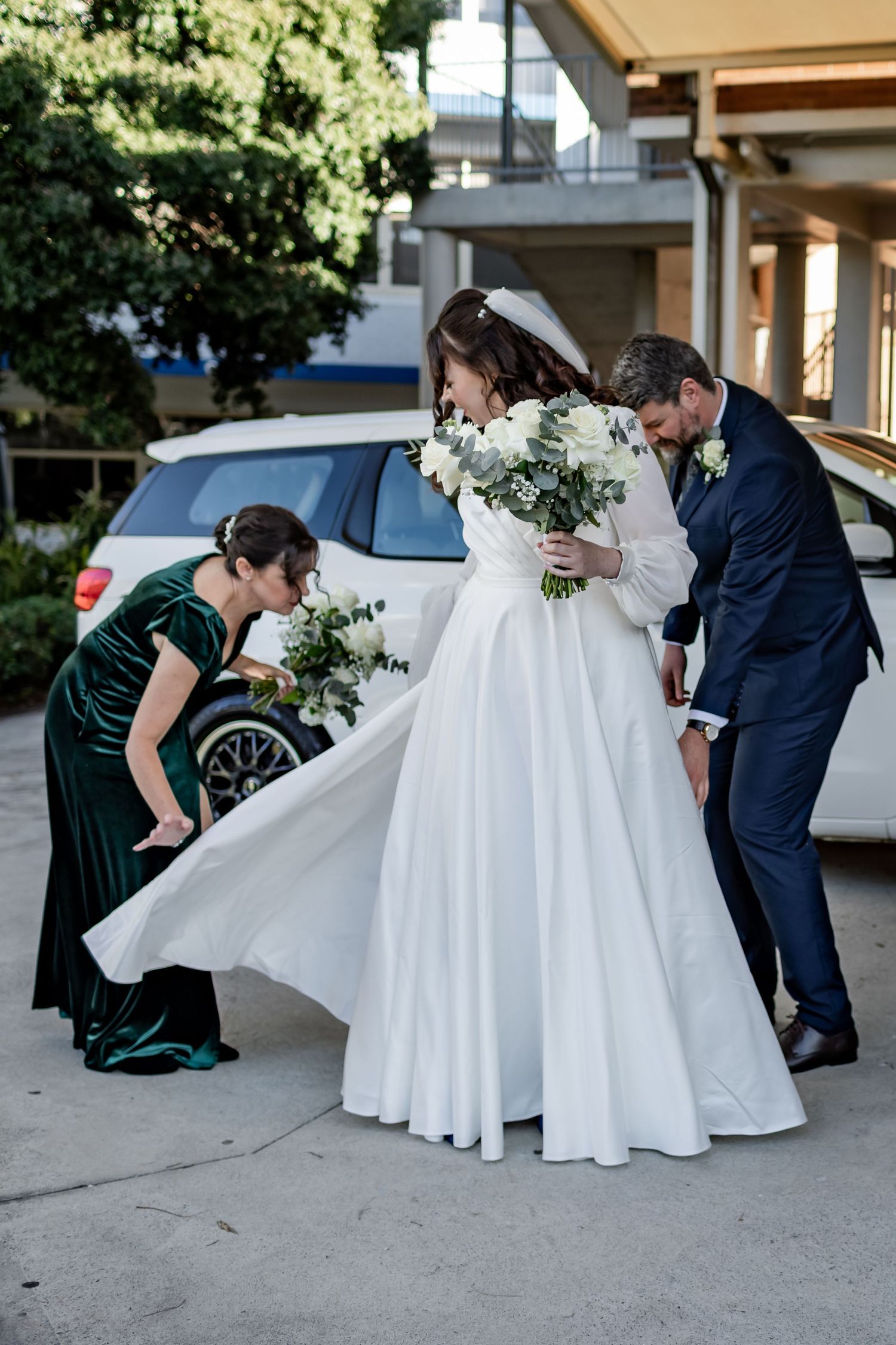 Wedding party helps adjust a bride's flowing white dress outdoors.
