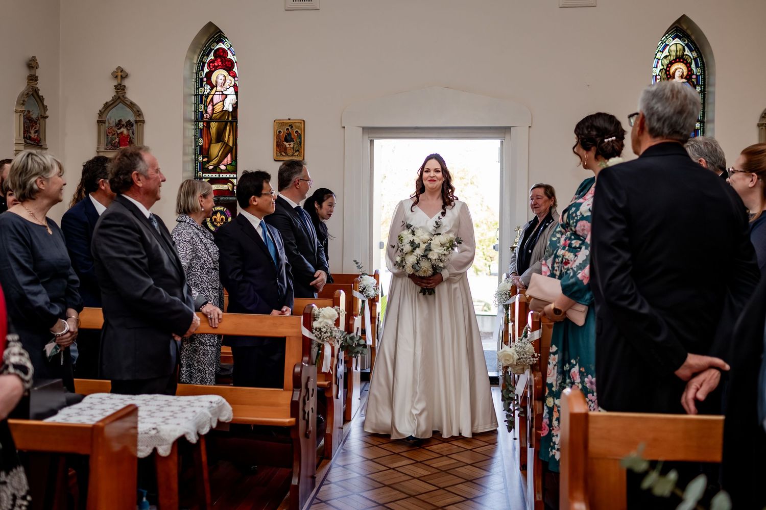 Wedding ceremony in progress inside church with stained glass windows and wooden pews.