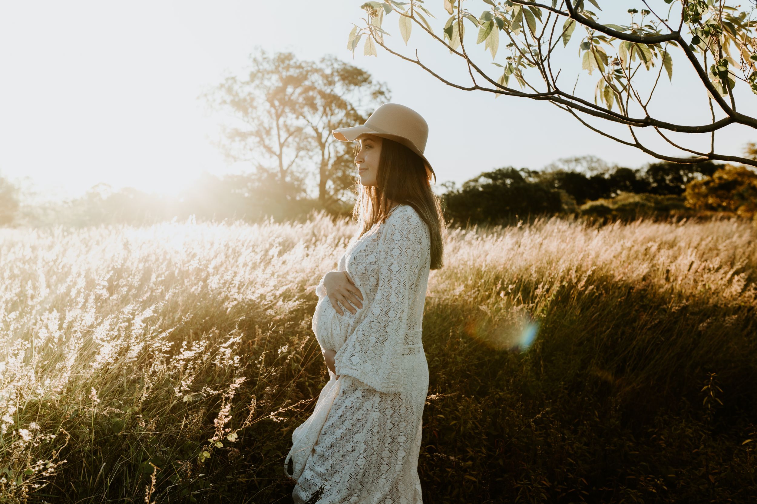 A silhouetted figure in a white dress stands in a sun-drenched field of tall grass.