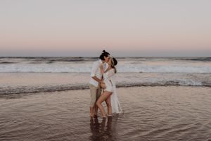 A romantic beach photoshoot at sunset with waves crashing in the background.