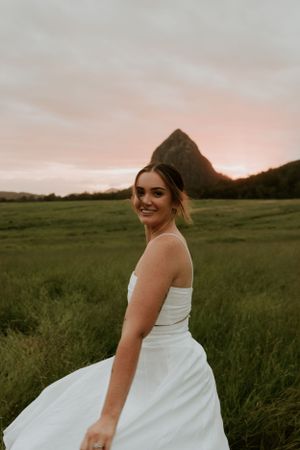 A bride in white dress poses in front of mountain landscape at sunset.