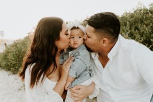 A tender family moment with parents kissing their baby outdoors.