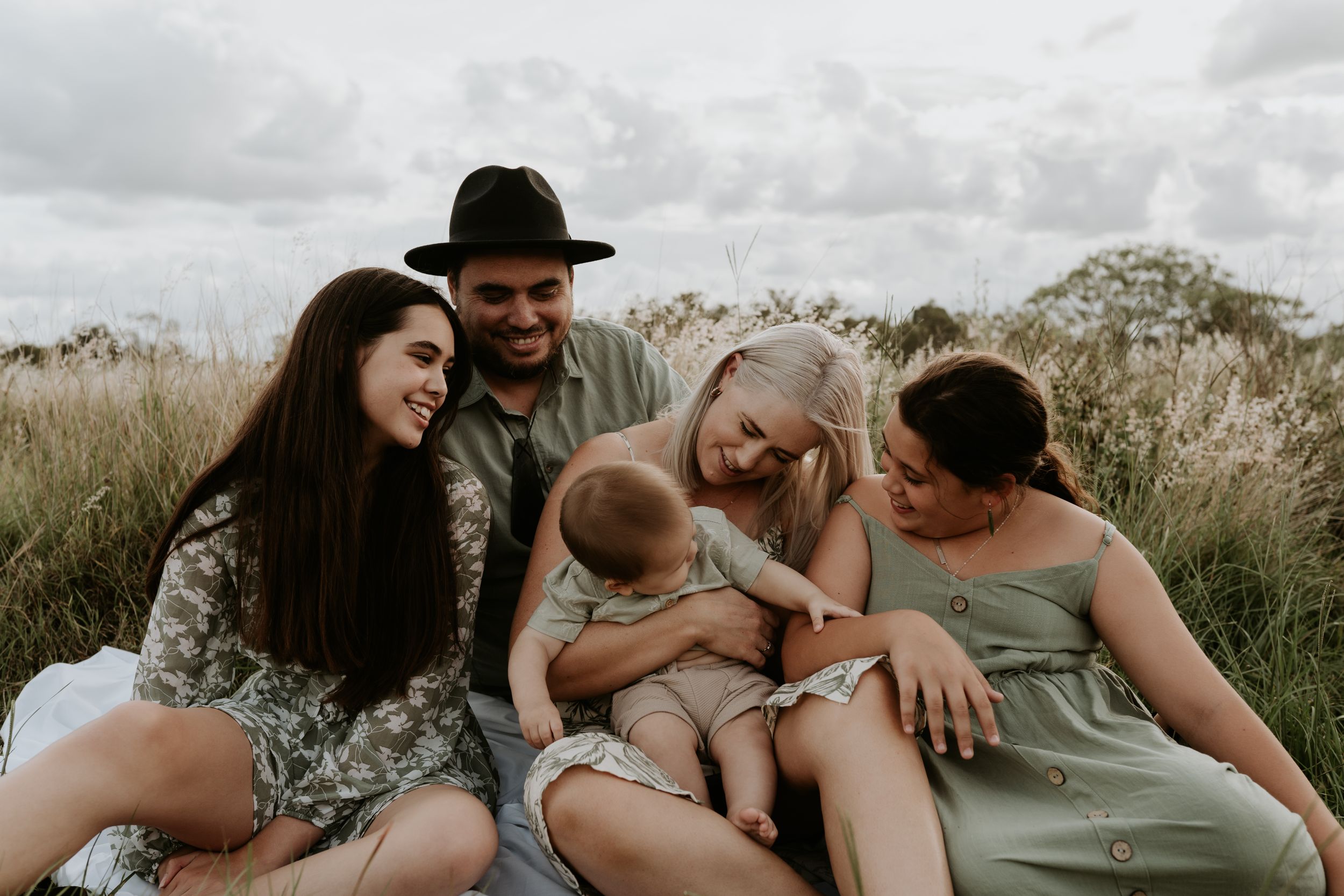 Friends gather in tall grass field for intimate group photo with baby.
