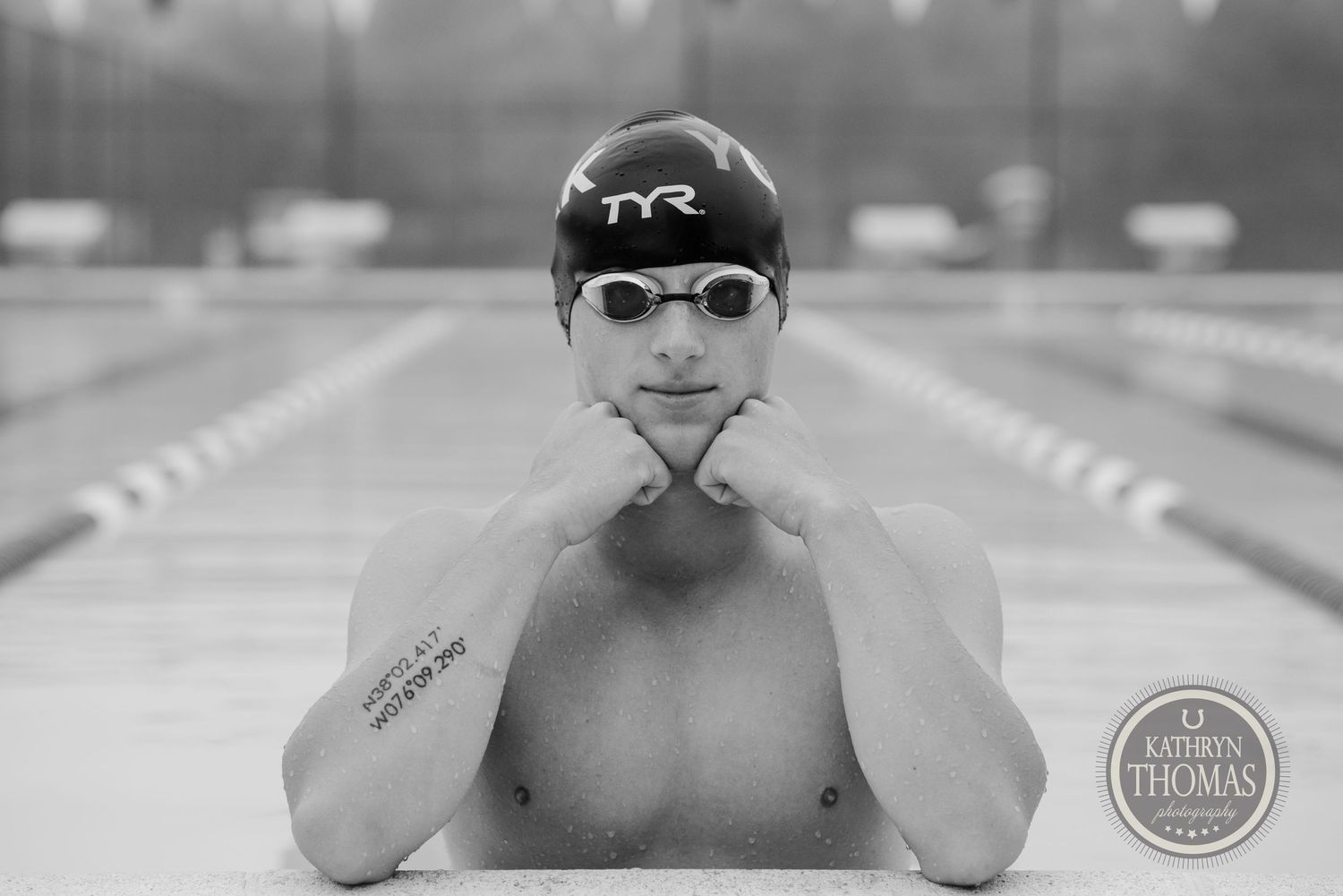 A competitive swimmer in TYR cap and goggles poses at the edge of a swimming pool.