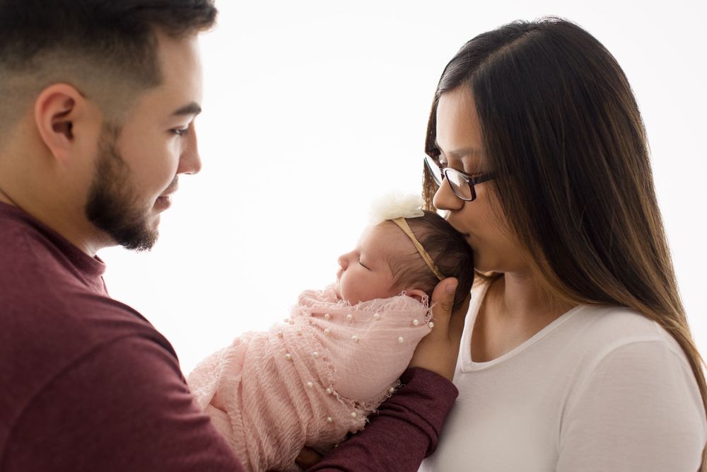 Intimate newborn family moment against white backdrop.