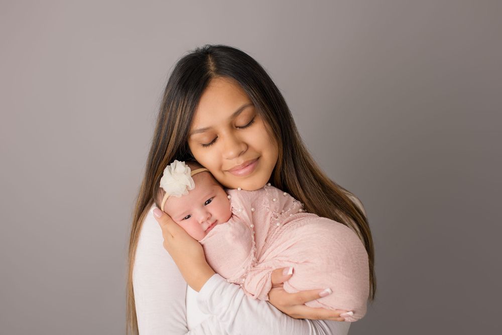 A tender moment of embrace between parent and newborn baby wrapped in pink against a gray background.